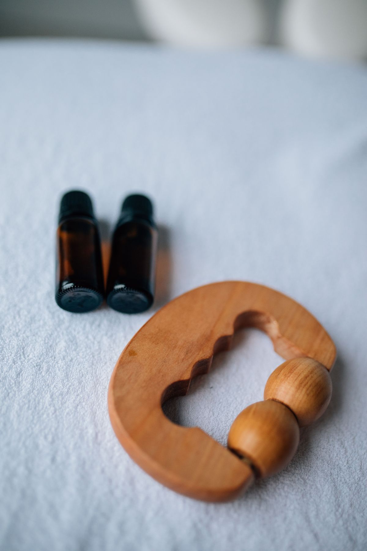 Essential oil bottles and a wooden massage roller on fresh linen